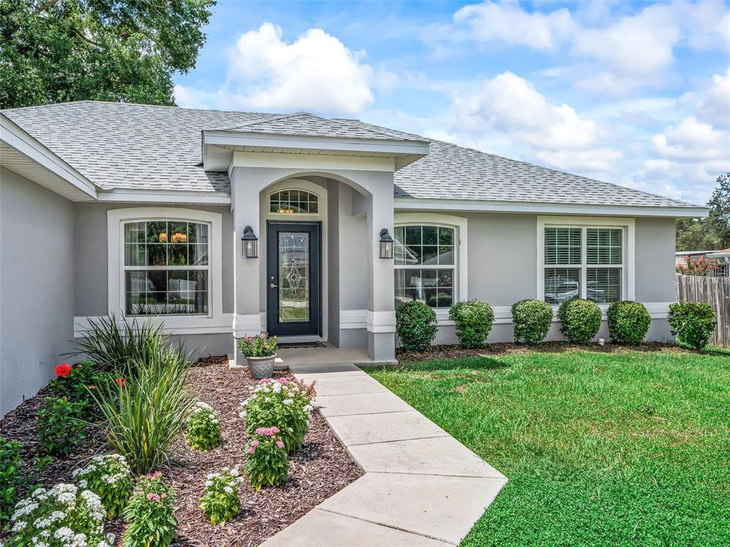 A single-story house with a gray exterior, a front walkway, and a landscaped garden — 9312 SE 162ND PLACE, SUMMERFIELD, FL