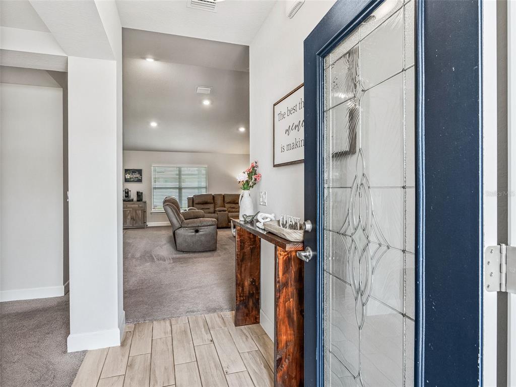 An entryway with tile flooring leads into a carpeted living room with a recliner — 9312 SE 162ND PLACE, SUMMERFIELD, FL