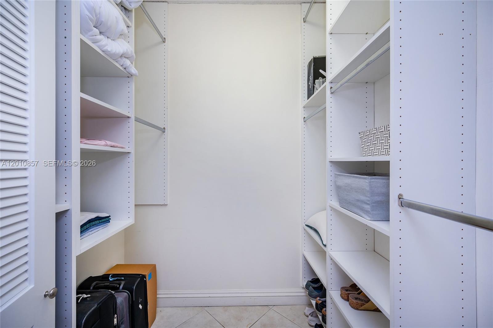 A walk-in closet features white shelving units, hanging rods, and tile flooring — 201 Crandon Blvd # 505, Key Biscayne FL 33149, KEY BISCAYNE, FL