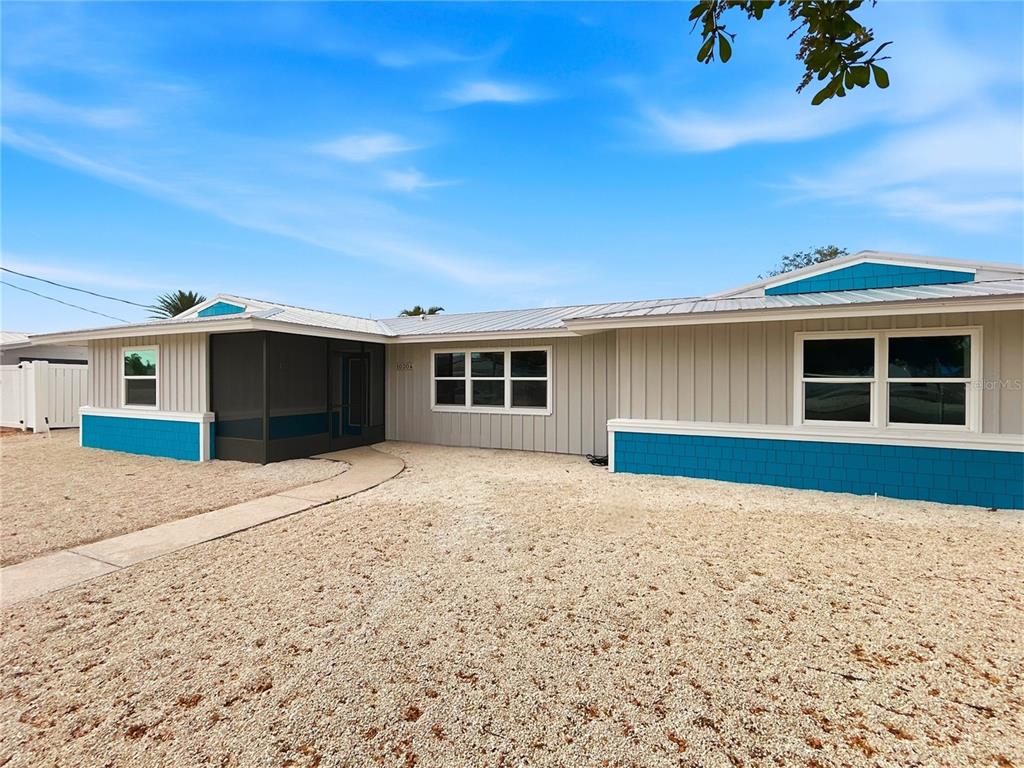 A single-story house features gray vertical siding, blue accents, and a gravel front yard — 10304 KINGFISHER ROAD W, BRADENTON, FL