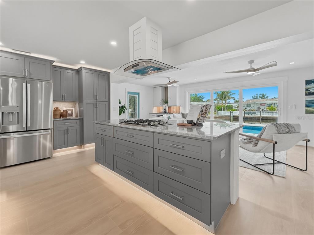 A modern kitchen features gray cabinets, a large island with a cooktop, and water views — 10304 KINGFISHER ROAD W, BRADENTON, FL