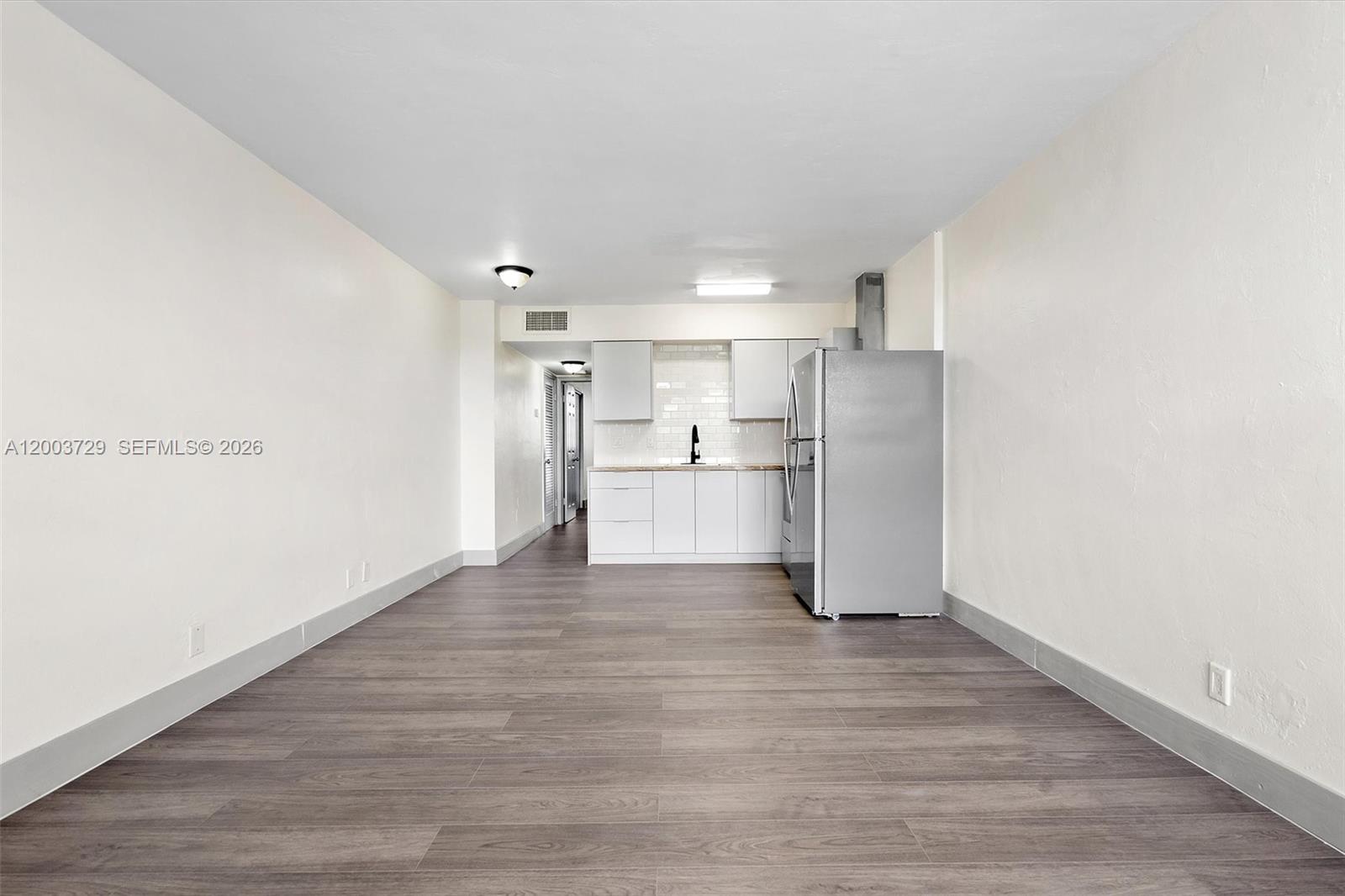 This room features a kitchen with white cabinets, a stainless steel refrigerator, and wood-look flooring — 1715 N 16th Ave # 111, Hollywood FL 33020, HOLLYWOOD, FL