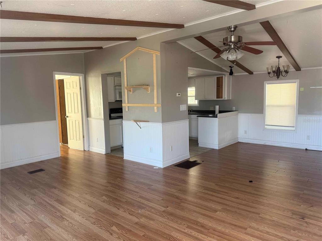 A living room with wood-look flooring, exposed ceiling beams, and a partial wall divider — 4008 PINE LANE, HAINES CITY, FL