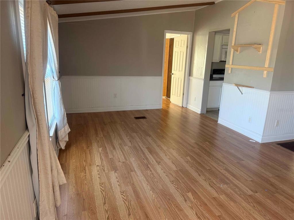 An interior room features wood-look flooring, white wainscoting, and a doorway leading to a kitchen — 4008 PINE LANE, HAINES CITY, FL