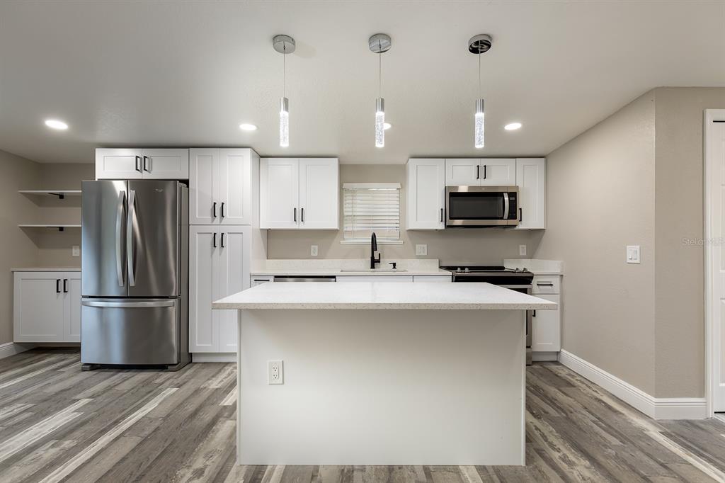 A modern kitchen features white cabinets, stainless steel appliances, a center island, and wood-look flooring — 1007 SAN DOMINGO ROAD, ORLANDO, FL