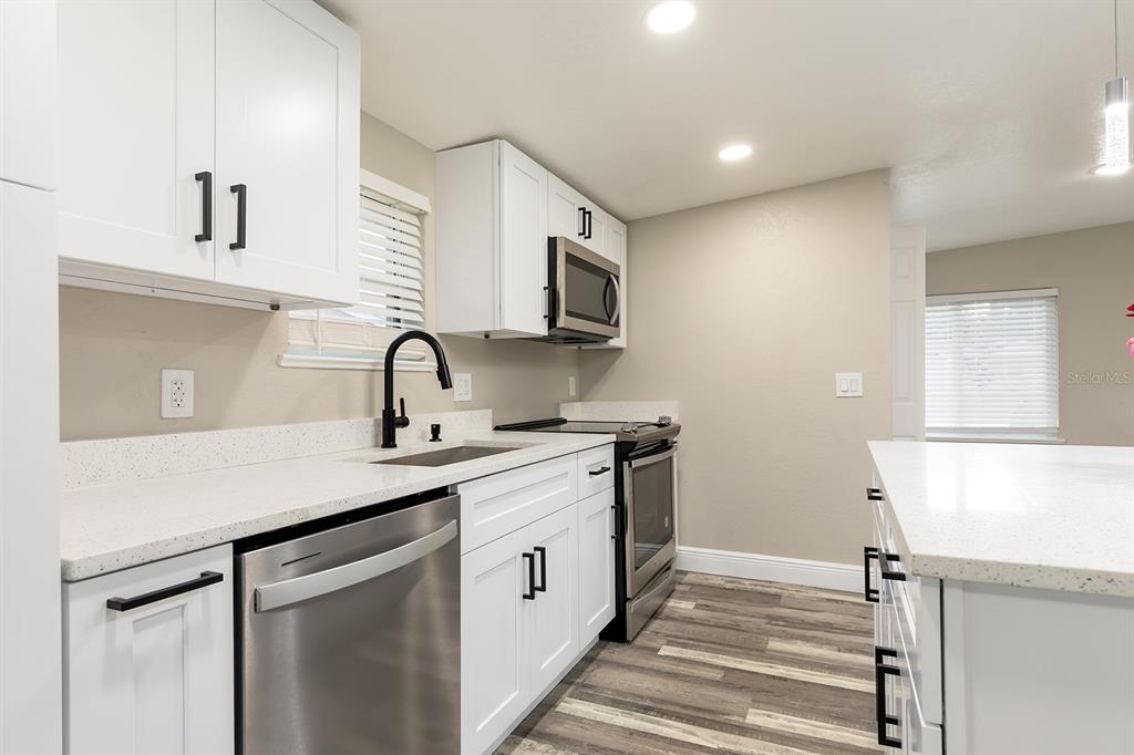 A modern kitchen features white cabinets, stainless steel appliances, quartz countertops, and wood-look flooring — 1007 SAN DOMINGO ROAD, ORLANDO, FL