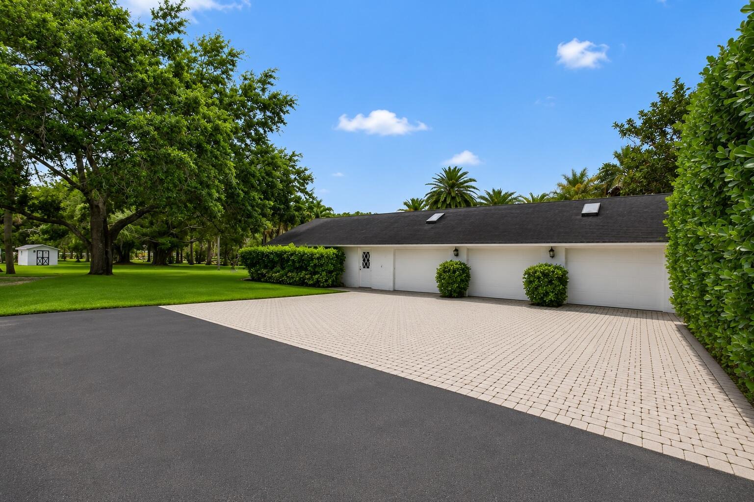 A paved driveway leads to a three-car garage with a black roof and landscaping — 1030 Arabian Drive, Loxahatchee FL 33470, LOXAHATCHEE, FL