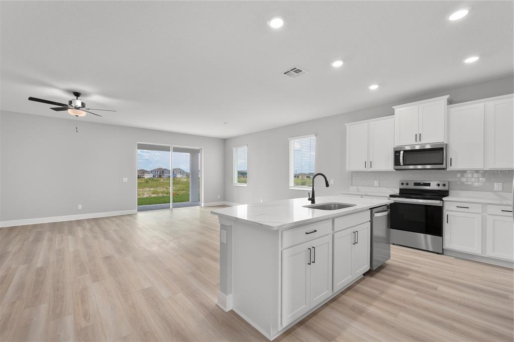 A modern kitchen with white cabinets and a center island opens to a living area — 3360 CHINOTTO DRIVE, LAKE ALFRED, FL
