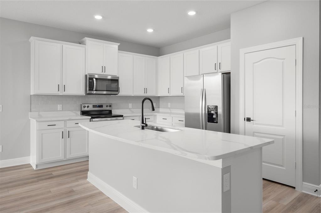 A modern kitchen features white cabinets, stainless steel appliances, and a central quartz island — 3360 CHINOTTO DRIVE, LAKE ALFRED, FL