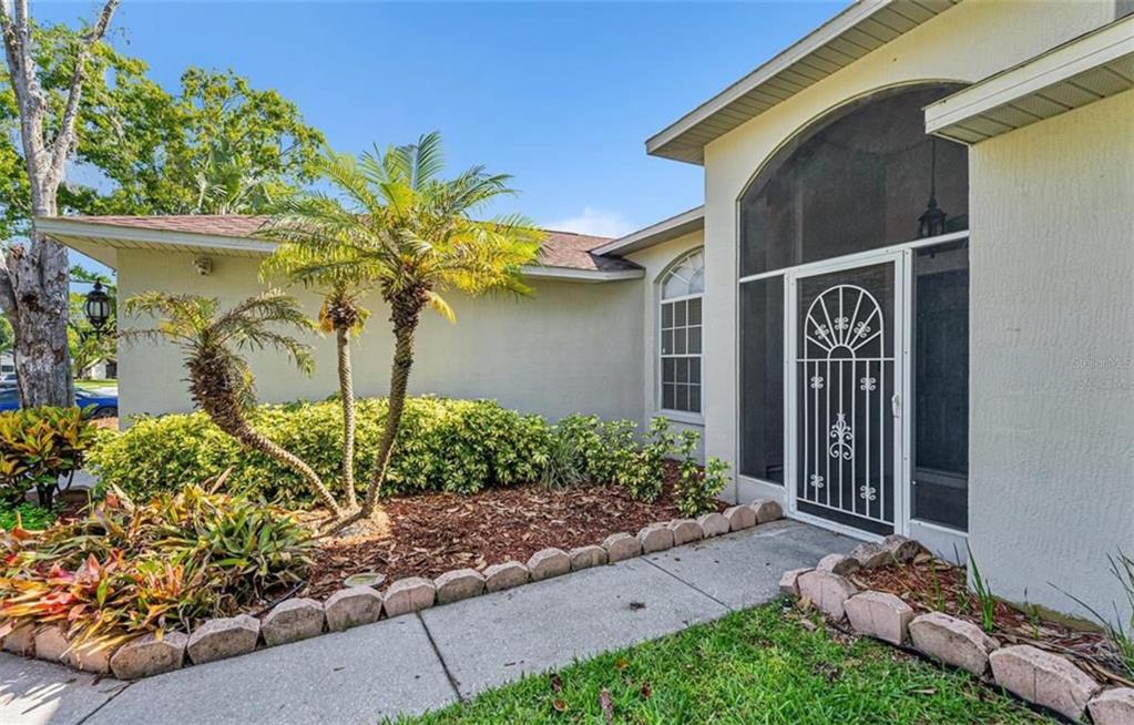 A paved walkway leads to the front entrance of a house with a screened door — 7330 FAIRWOOD AVENUE, NEW PORT RICHEY, FL