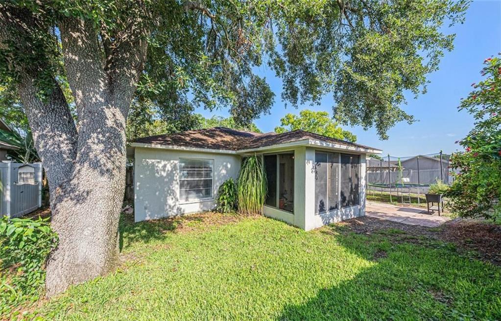 The exterior of a house features a screened-in porch, a large tree, and grassy yard — 7330 FAIRWOOD AVENUE, NEW PORT RICHEY, FL