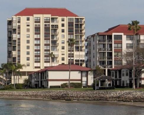 A multi-story apartment complex with red roofs sits along a rocky shoreline — 6279 SUN BOULEVARD UNIT 604, ST PETERSBURG, FL