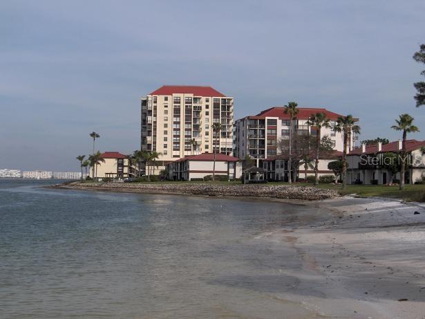 A multi-story apartment complex sits along a sandy beach with palm trees and water — 6279 SUN BOULEVARD UNIT 604, ST PETERSBURG, FL