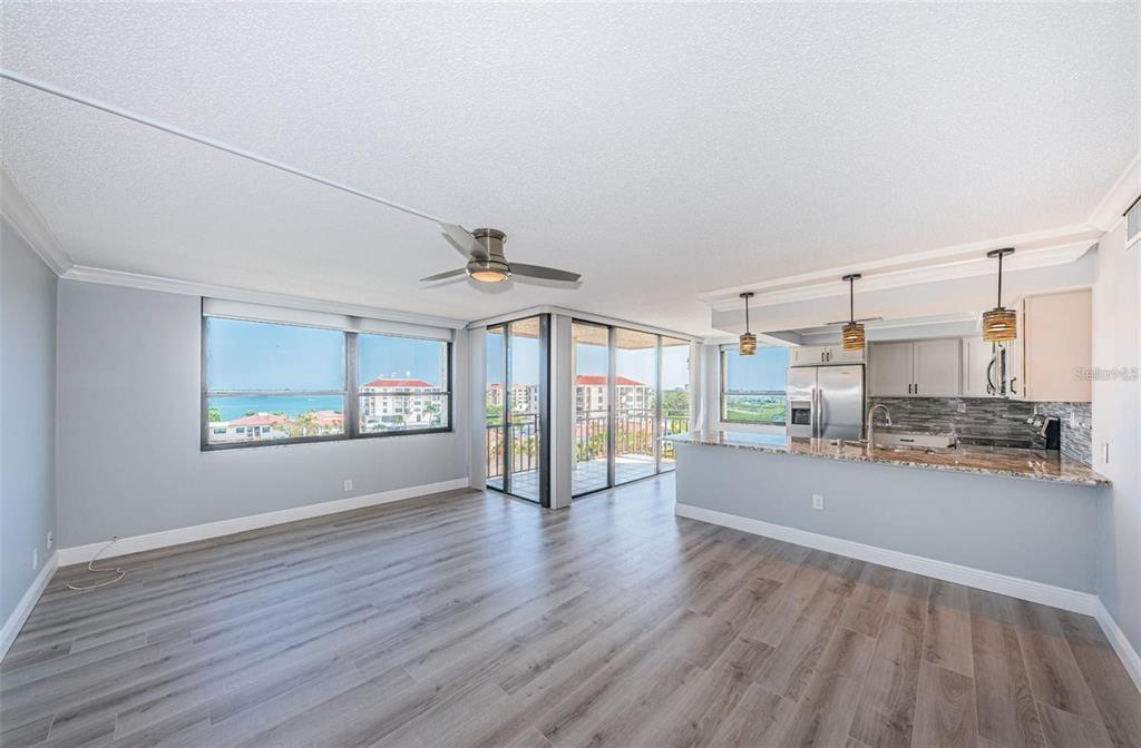 An open-concept living area with gray wood-look flooring, a kitchen island, and a balcony view — 6279 SUN BOULEVARD UNIT 604, ST PETERSBURG, FL