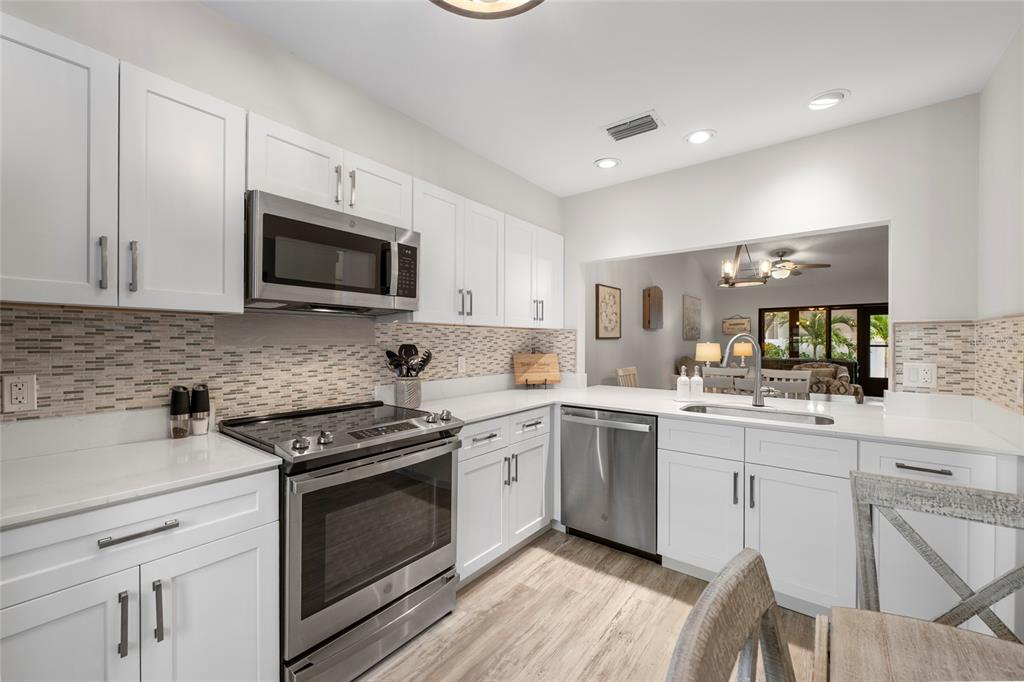 A kitchen features white cabinets, stainless steel appliances, quartz countertops, and a tiled backsplash — 6015 27TH STREET W UNIT 1C, BRADENTON, FL