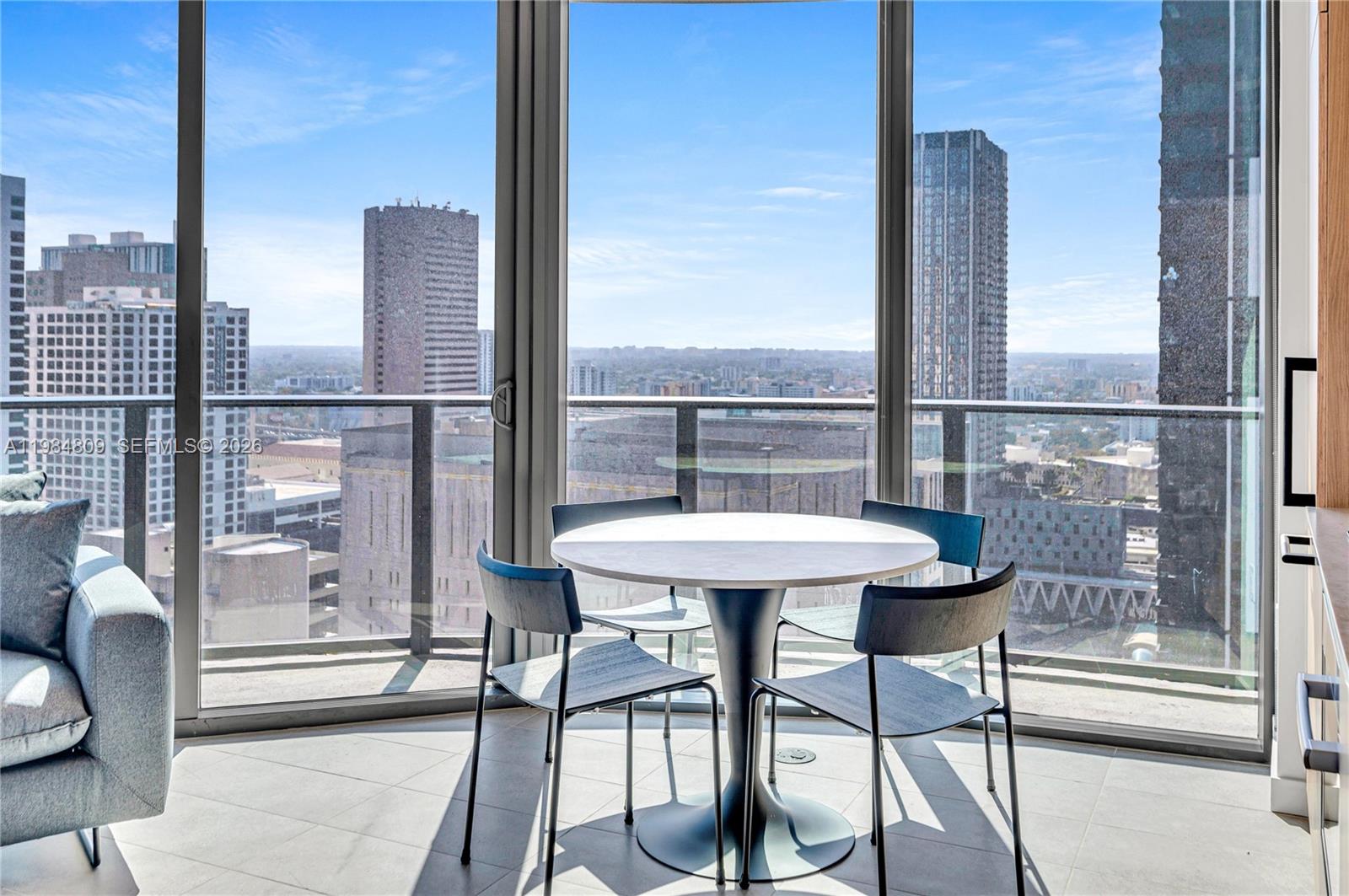 A dining area with a round table and four chairs sits before floor-to-ceiling city views — 121 NE 5th St # 3005, Miami FL 33130, MIAMI, FL