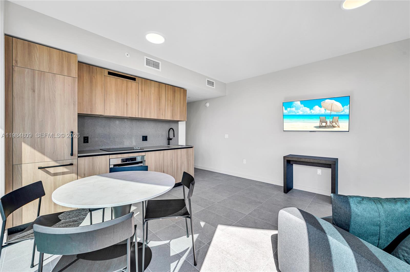 A modern studio apartment features a kitchenette with wood cabinets and a dining area — 121 NE 5th St # 3005, Miami FL 33130, MIAMI, FL