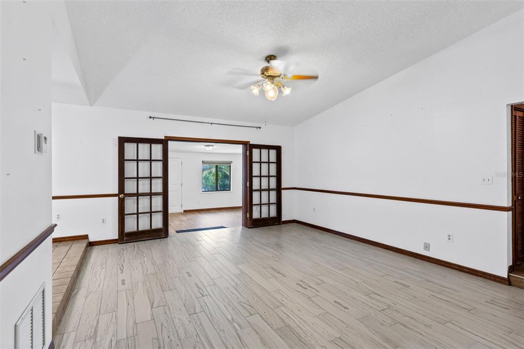 An empty room with light wood-look tile flooring, white walls, and dark wood French doors — 17531 N SUNSET TERRACE, WINTER GARDEN, FL