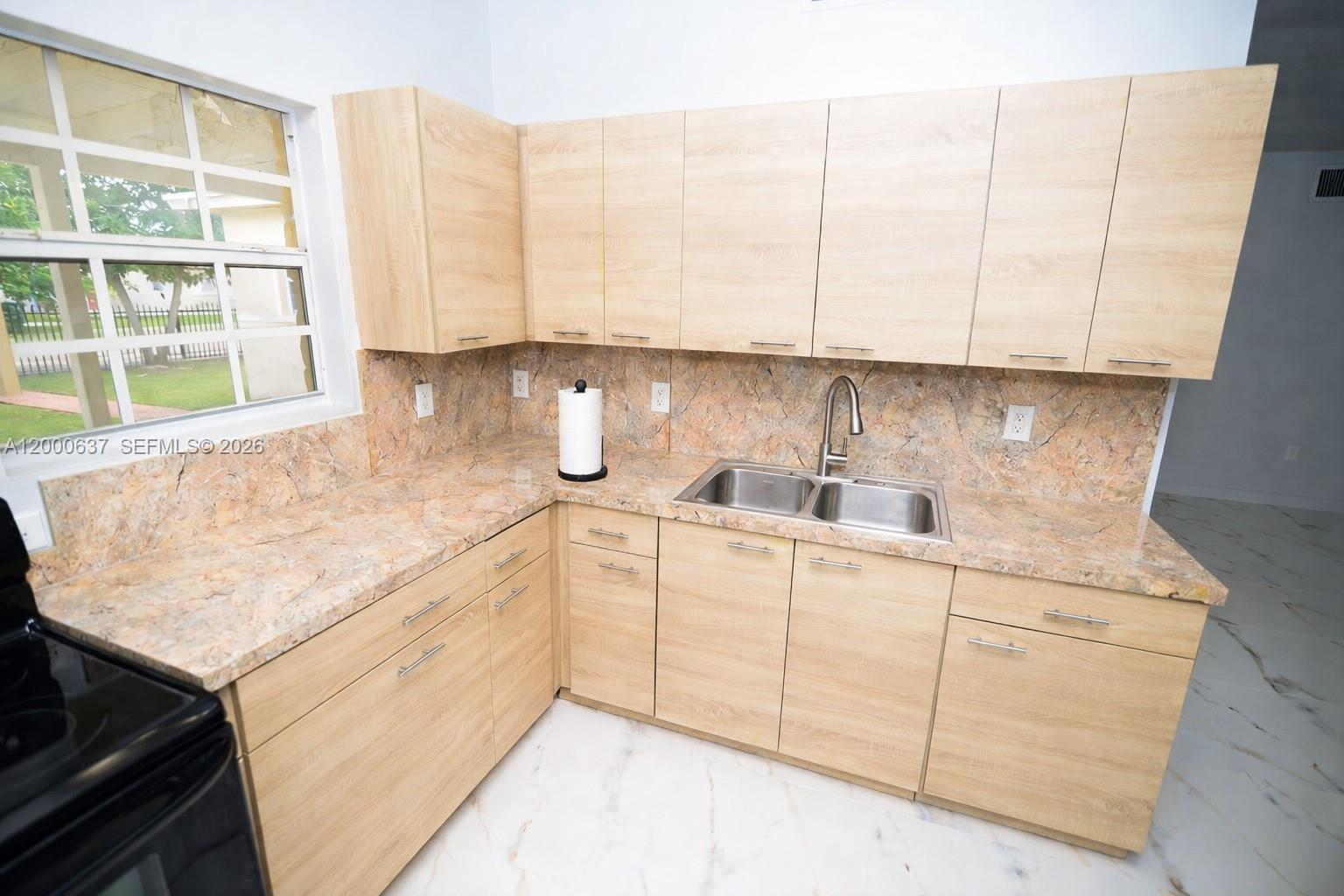 A kitchen features light wood cabinets, a stone-patterned countertop and backsplash, and a double sink — 298 NW 104th St, Miami FL 33150, MIAMI, FL