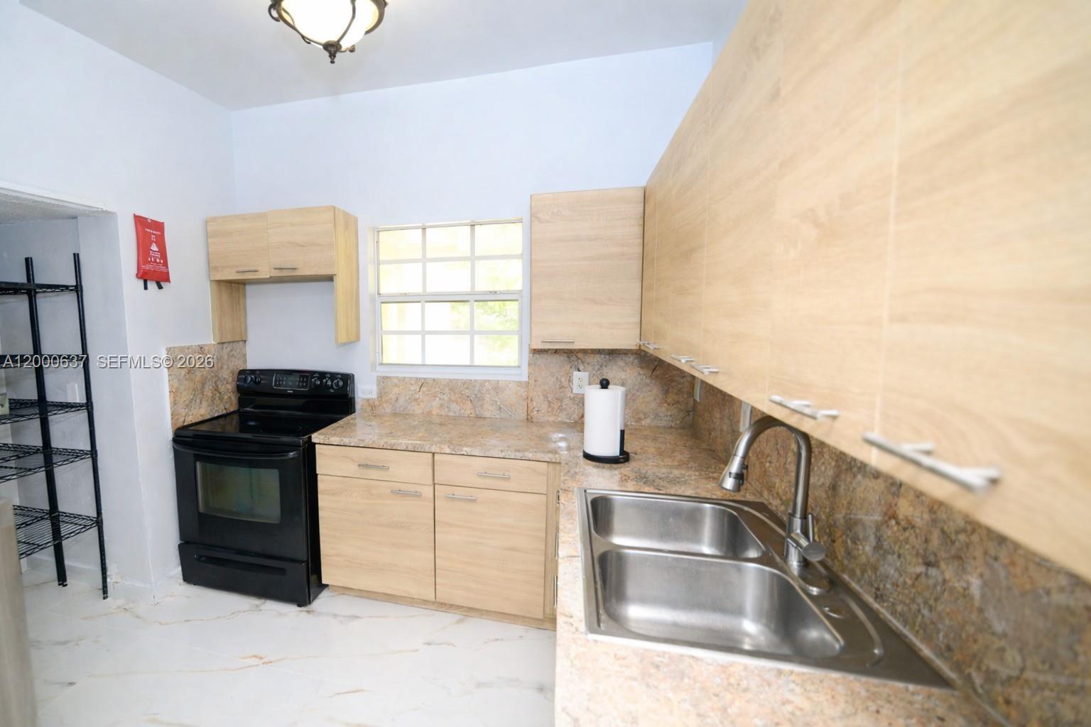 A kitchen features light wood cabinets, granite countertops, a black stove, and a double sink — 298 NW 104th St, Miami FL 33150, MIAMI, FL