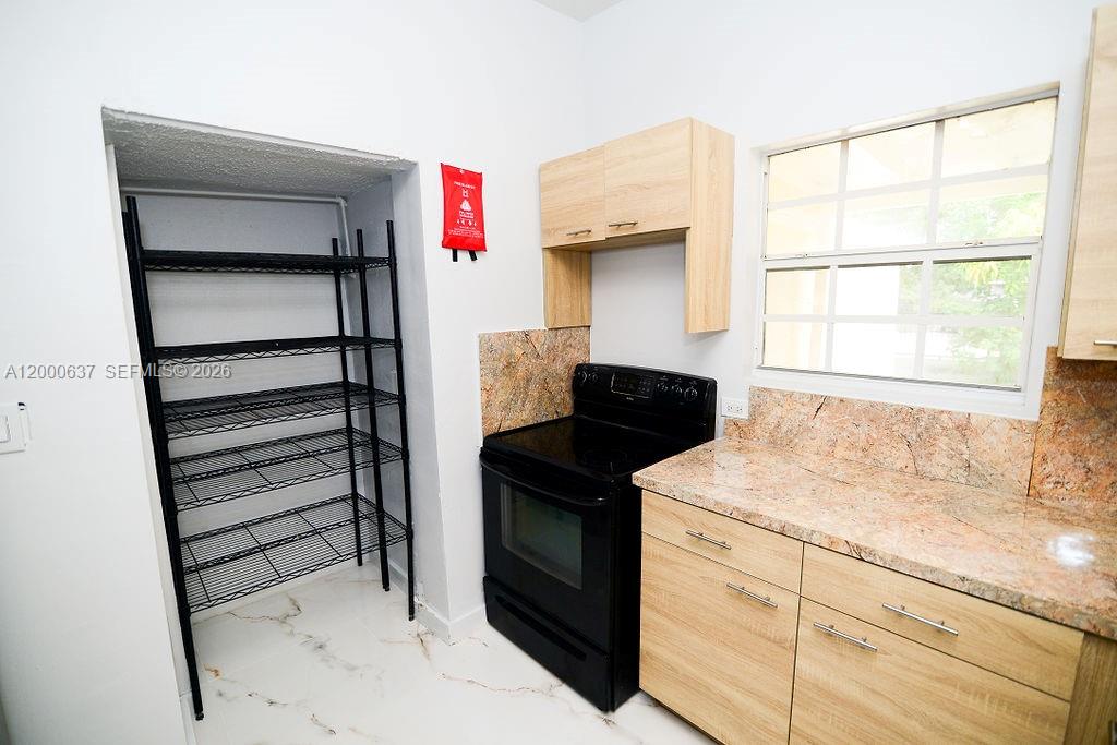 A kitchen features light wood cabinets, granite countertops, a black stove, and a wire shelving unit — 298 NW 104th St, Miami FL 33150, MIAMI, FL