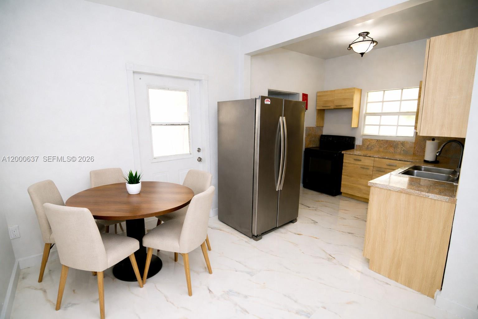 A kitchen and dining area features light wood cabinets, stainless steel appliances, and marble-look flooring — 298 NW 104th St, Miami FL 33150, MIAMI, FL