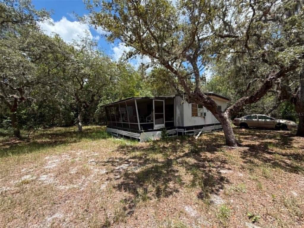 A single-story mobile home with a screened-in porch sits on a wooded, grassy lot — 10051 WADDELL STREET, NEW PORT RICHEY, FL
