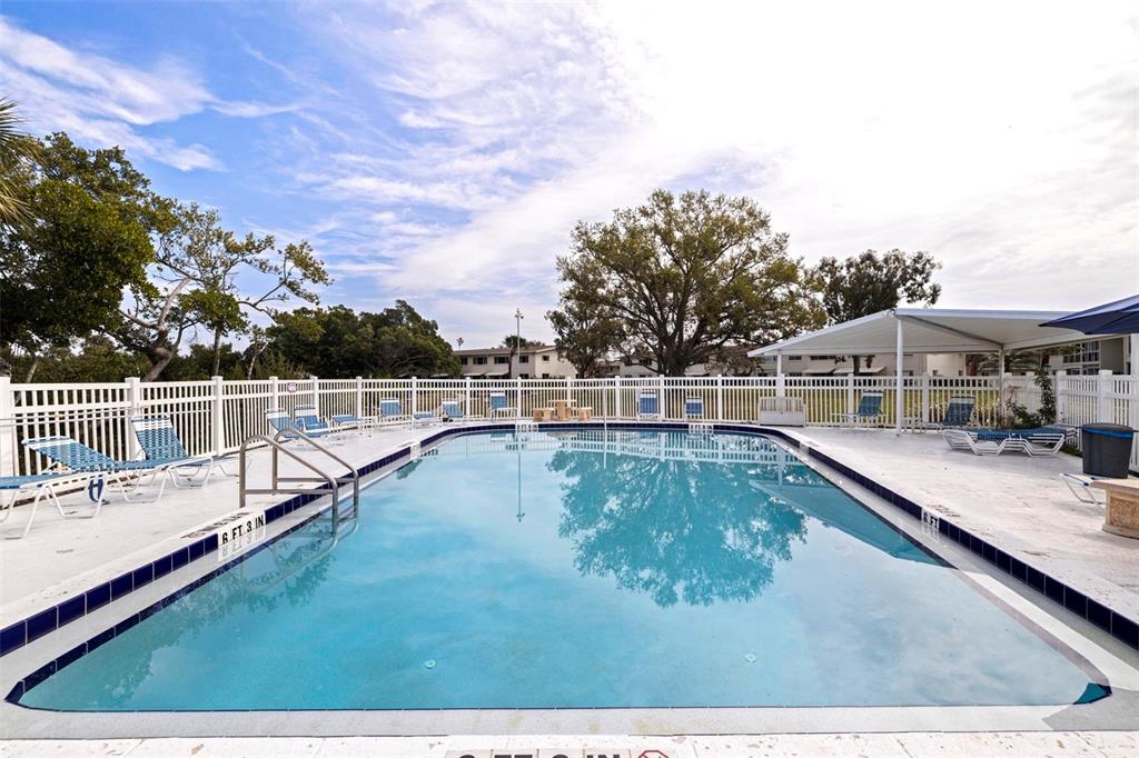 An outdoor swimming pool is surrounded by a white fence, lounge chairs, and trees — 4480 OVERLOOK DRIVE NE UNIT 10, ST PETERSBURG, FL