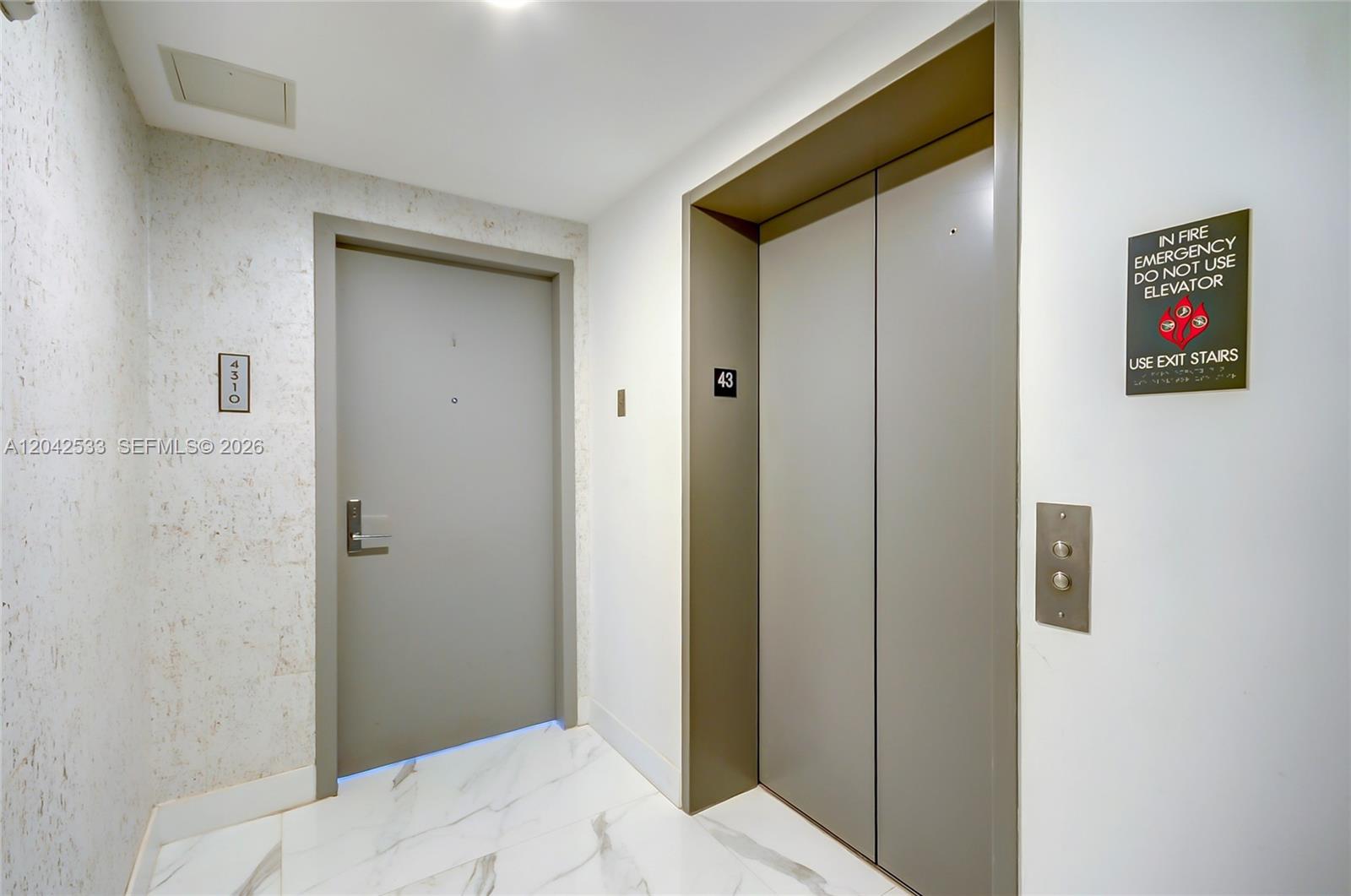 A gray apartment door stands next to an elevator in a white-walled hallway — 488 NE 18th St # 4310, Miami FL 33132, MIAMI, FL