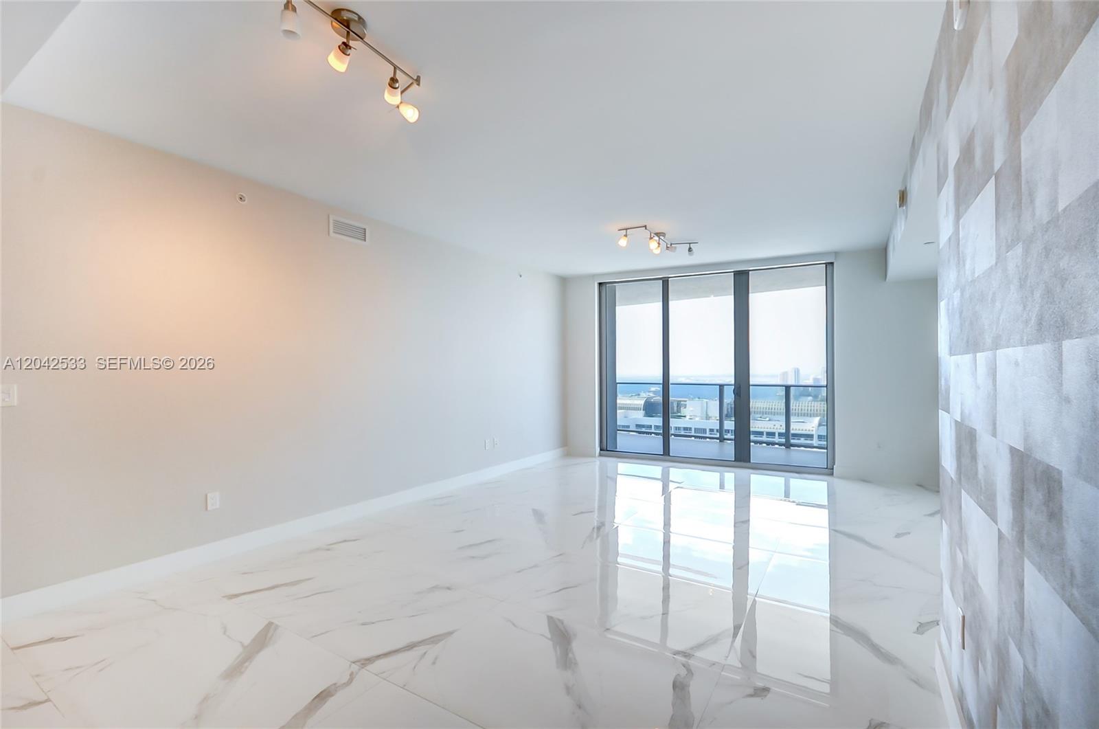A bright, empty living room features white marble floors, track lighting, and floor-to-ceiling balcony windows — 488 NE 18th St # 4310, Miami FL 33132, MIAMI, FL