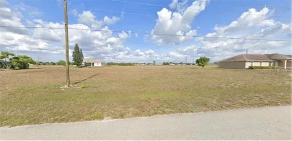 A vacant, grassy lot sits next to a suburban house under a cloudy sky — 2727 NW JUANITA PLACE, CAPE CORAL, FL