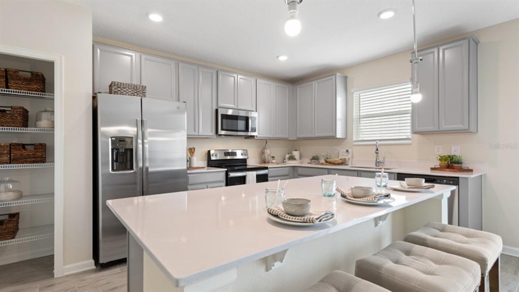 A kitchen features gray cabinets, stainless steel appliances, a large island, and an adjacent pantry — 5221 WORCHESTER DRIVE, KISSIMMEE, FL