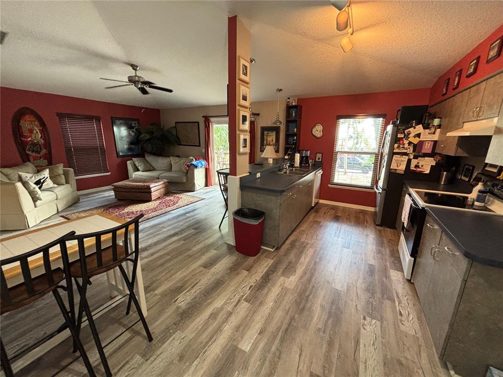 An open-concept kitchen and living area features wood-look flooring, red accent walls, and gray cabinetry — 716 32ND STREET COURT E, BRADENTON, FL