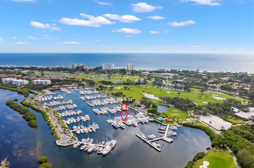 An aerial view shows a marina with numerous boats docked in slips near a golf course — 2600 HARBOURSIDE DRIVE UNIT B-13, LONGBOAT KEY, FL