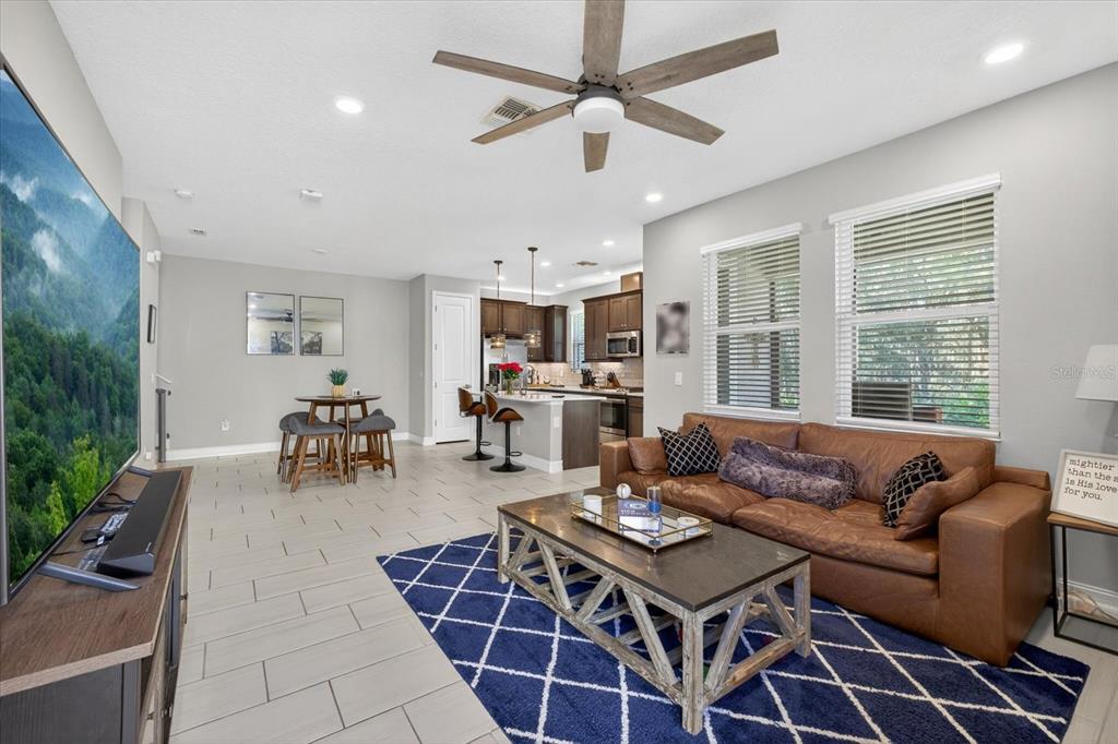An open-concept living room and kitchen featuring tile floors, a brown leather sofa, and island — 5110 SAN MARTINO DRIVE, WESLEY CHAPEL, FL