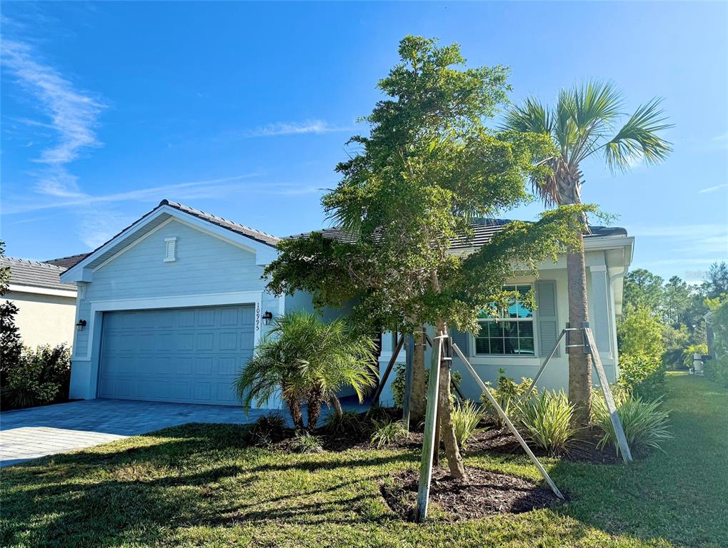 A light blue single-story house with a two-car garage and a front yard with trees — 10995 PINOT DRIVE, VENICE, FL