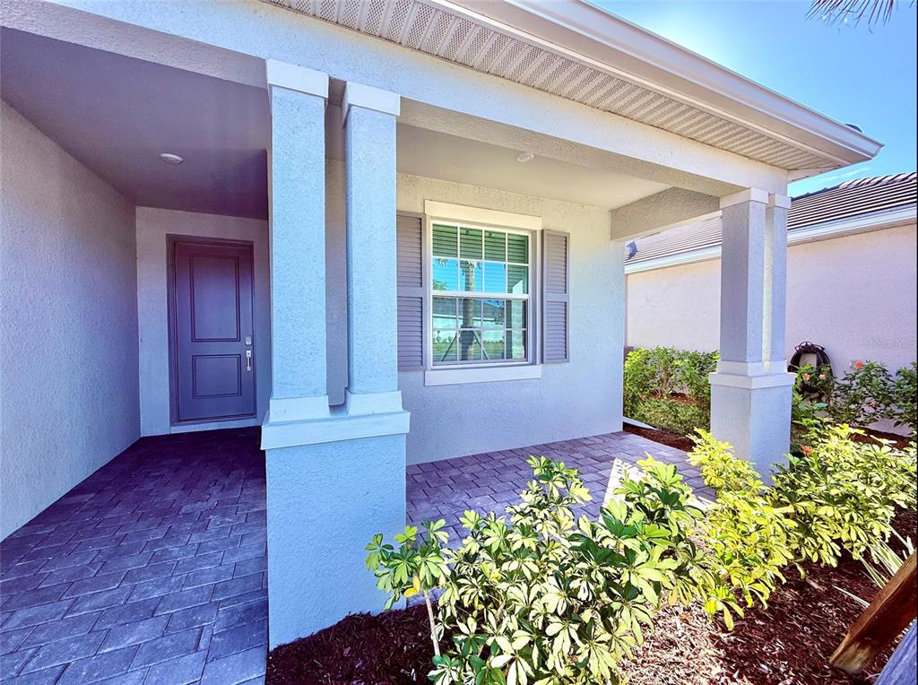 A covered front porch with a paved floor, columns, and a window with gray shutters — 10995 PINOT DRIVE, VENICE, FL