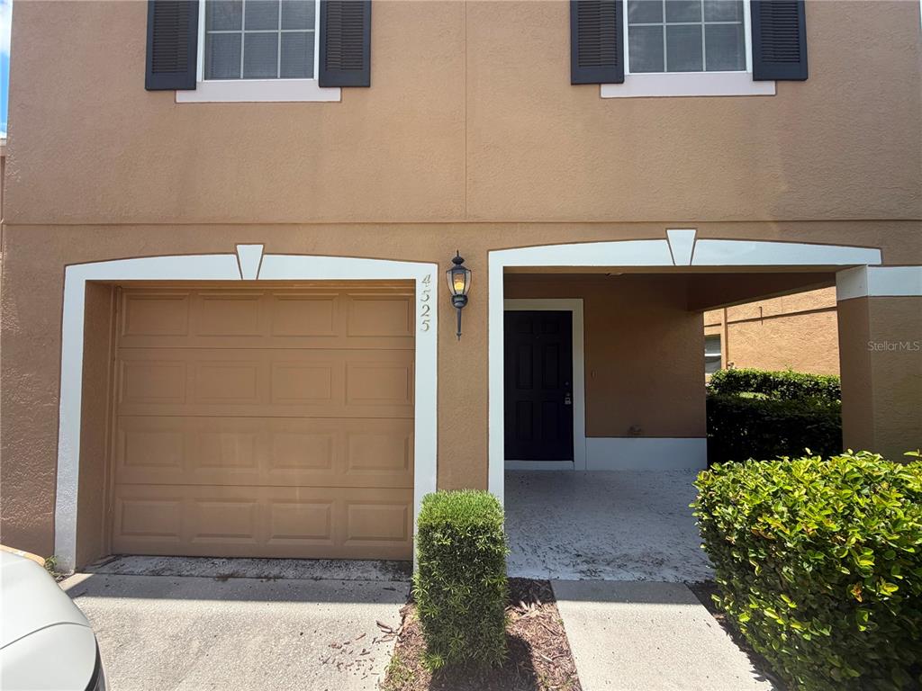 A tan two-story townhouse exterior features a single-car garage and a recessed front entrance — 4525 WINDING RIVER WAY, LAND O LAKES, FL