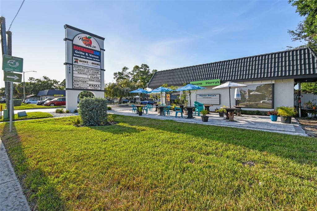 A commercial plaza building features an outdoor patio with tables and umbrellas under a roof — 14219 WALSINGHAM ROAD UNIT M, LARGO, FL