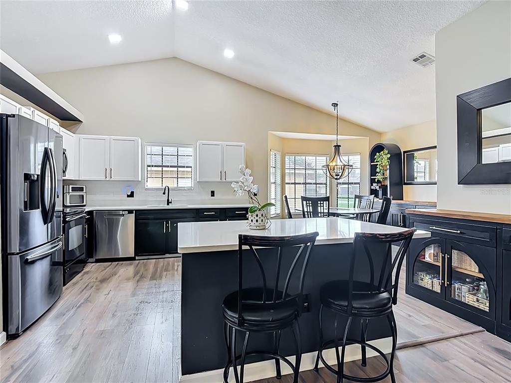 A kitchen features white upper cabinets, black lower cabinets, a central island, and wood-look flooring — 1393 WOOD LAKE CIRCLE, ST CLOUD, FL