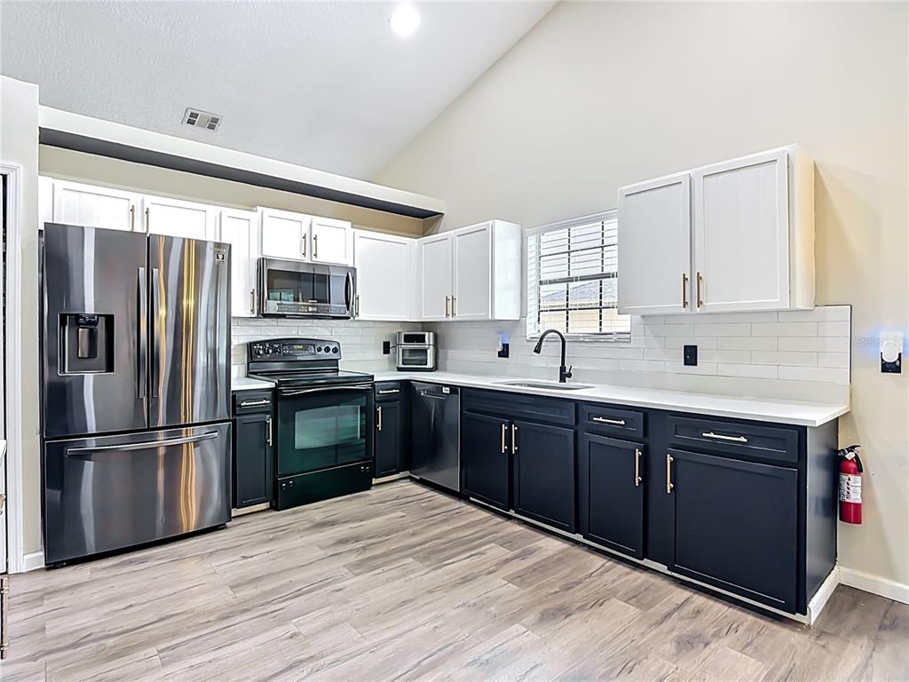 A kitchen features white upper cabinets, dark lower cabinets, stainless steel appliances, and wood-look flooring — 1393 WOOD LAKE CIRCLE, ST CLOUD, FL