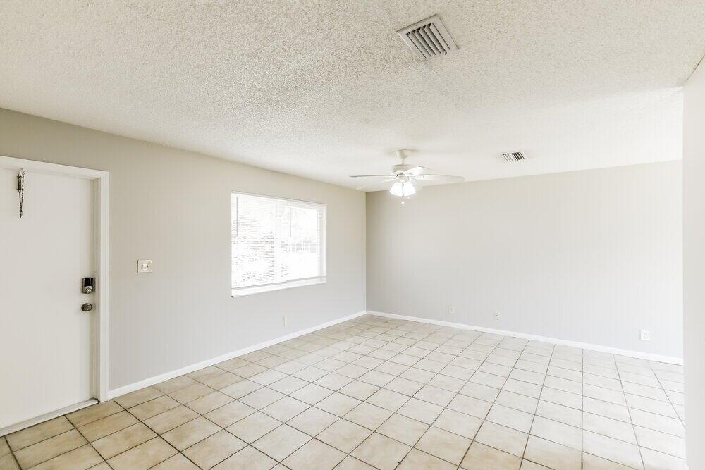 An empty living room with light gray walls, white trim, and beige tile flooring — NORTH LAUDERDALE, FL