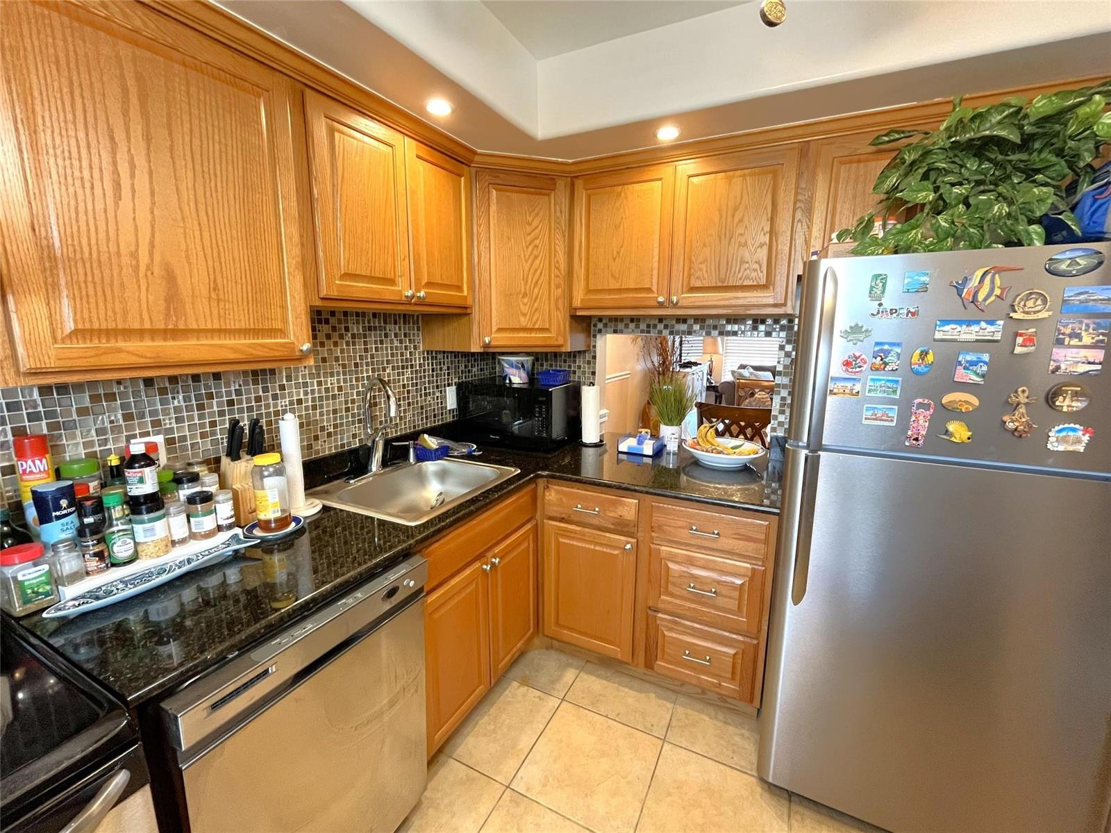 A kitchen features oak cabinets, black granite countertops, stainless steel appliances, and a tiled backsplash — 7837 Golf Circle Drive # 206, Margate FL 33063, MARGATE, FL