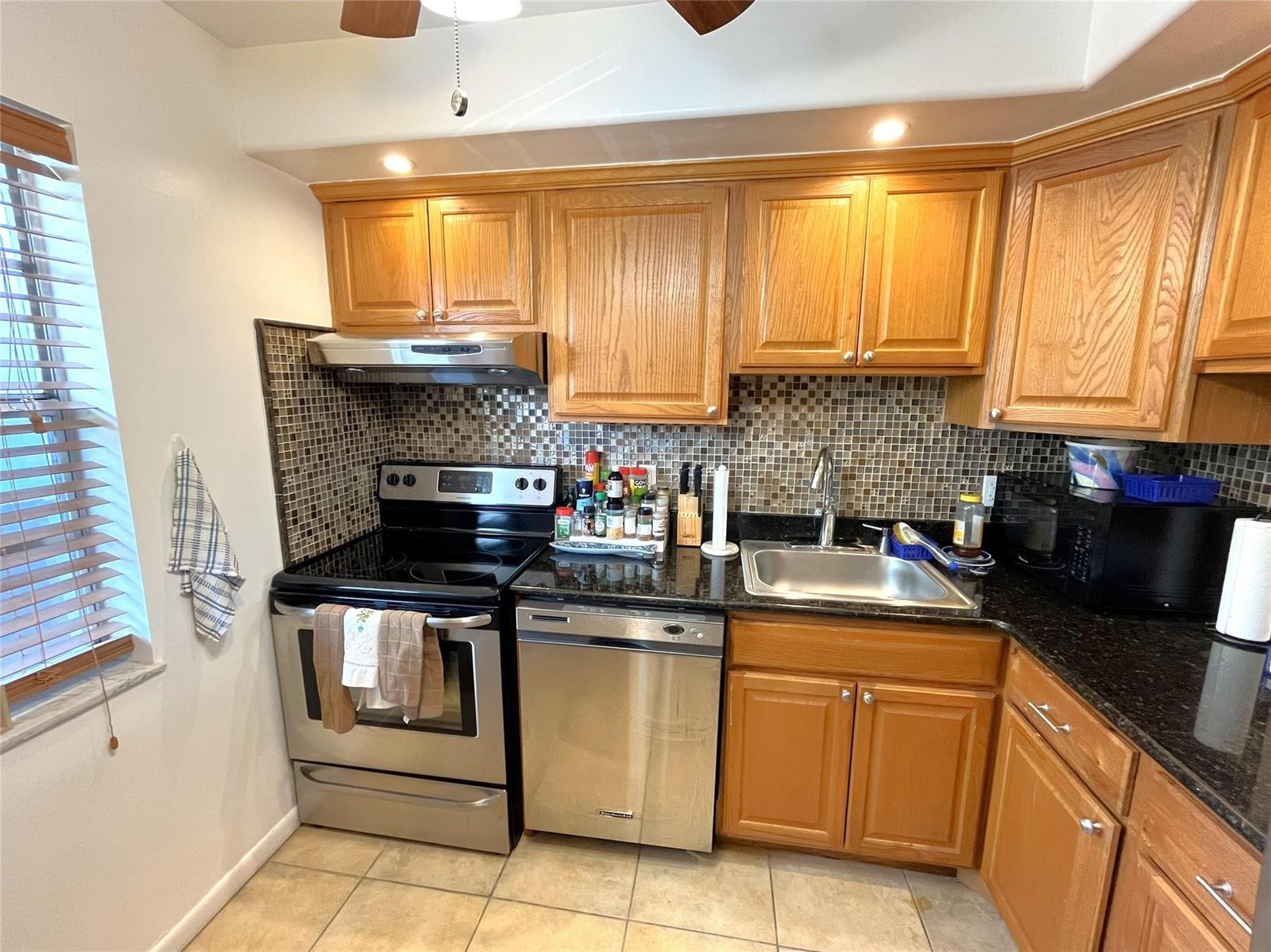A kitchen features wood cabinets, black granite countertops, stainless steel appliances, and a mosaic backsplash — 7837 Golf Circle Drive # 206, Margate FL 33063, MARGATE, FL