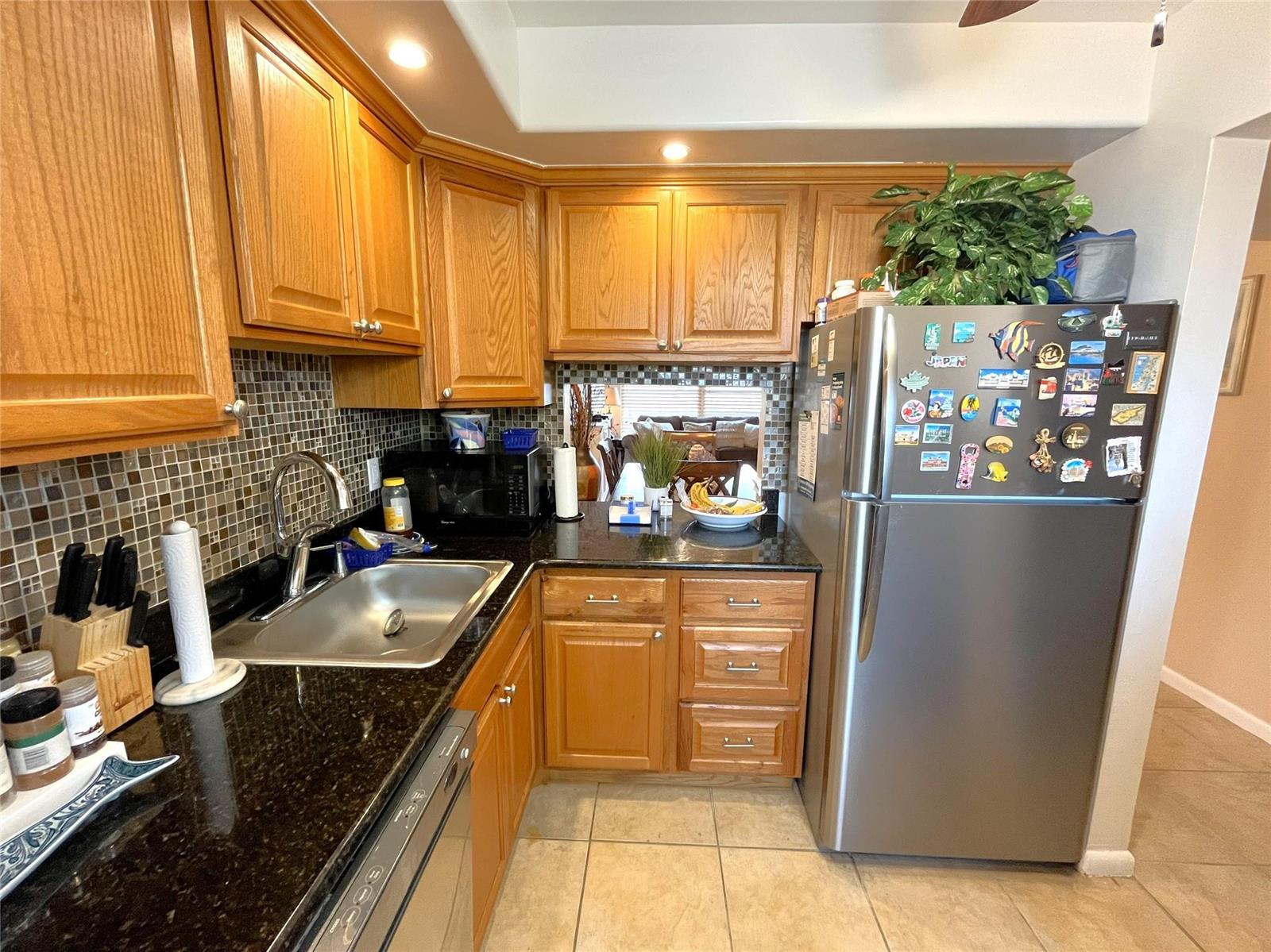 A kitchen features oak cabinets, black granite countertops, a stainless steel refrigerator, and tiled backsplash — 7837 Golf Circle Drive # 206, Margate FL 33063, MARGATE, FL