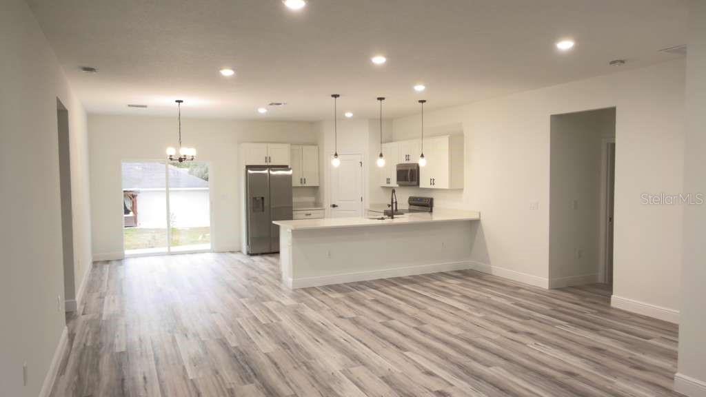 An open-concept kitchen and dining area features white cabinetry, stainless appliances, and wood-look flooring — 14905 SW 24TH CIRCLE, OCALA, FL