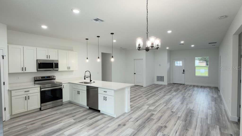 A modern kitchen with white cabinets, stainless steel appliances, and wood-look flooring — 14905 SW 24TH CIRCLE, OCALA, FL
