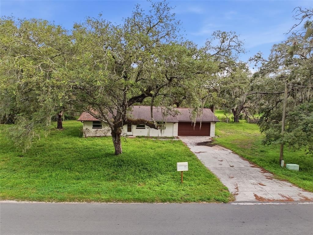 A single-story house with a brown roof and garage sits behind a large oak tree — 34696 ORCHID PARKWAY, DADE CITY, FL