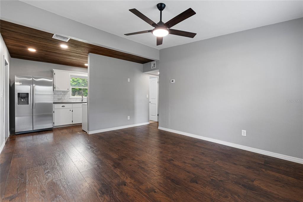 A living room with dark wood flooring, gray walls, and a ceiling fan opens to a kitchen — 460 E 3RD STREET, CHULUOTA, FL