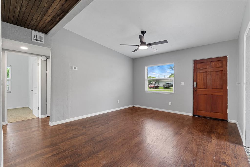 A living room with wood-look flooring, gray walls, a ceiling fan, and a wooden front door — 460 E 3RD STREET, CHULUOTA, FL
